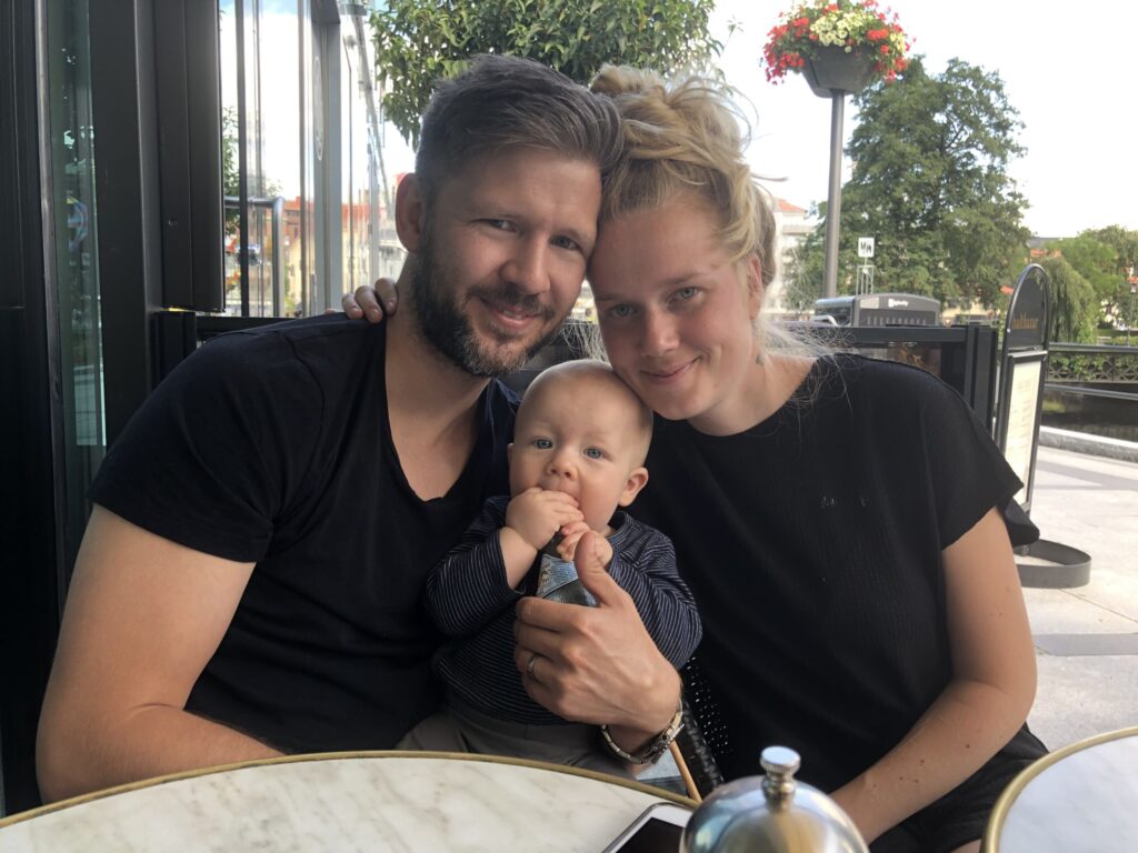 Johan Berg och hans fru Lina Berg sitter bredvid varandra med huvudena lutade mot varandra på en uteservering. Sonen Love sitter i deras knä.