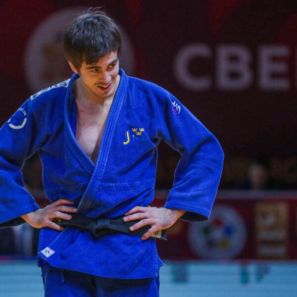 Tommy Macias i blå judodräkt står med armarna i sidan och tittar snett nedåt.