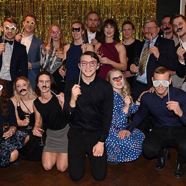 Gruppbild på festklädda personer utklädda med lösmustascher och hattar.