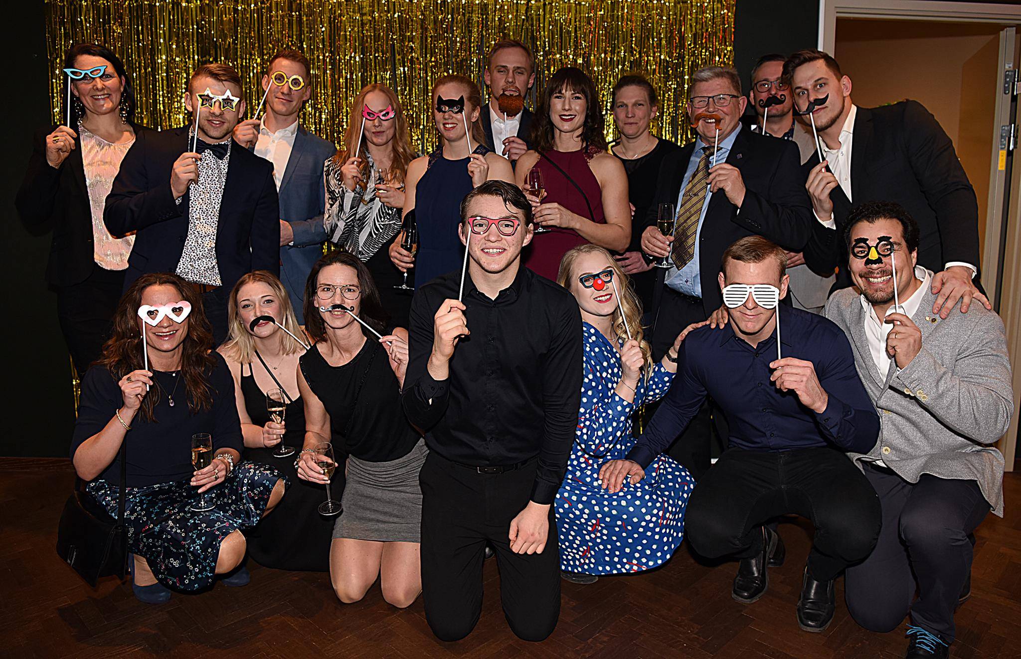 Gruppbild på festklädda personer utklädda med lösmustascher och hattar.